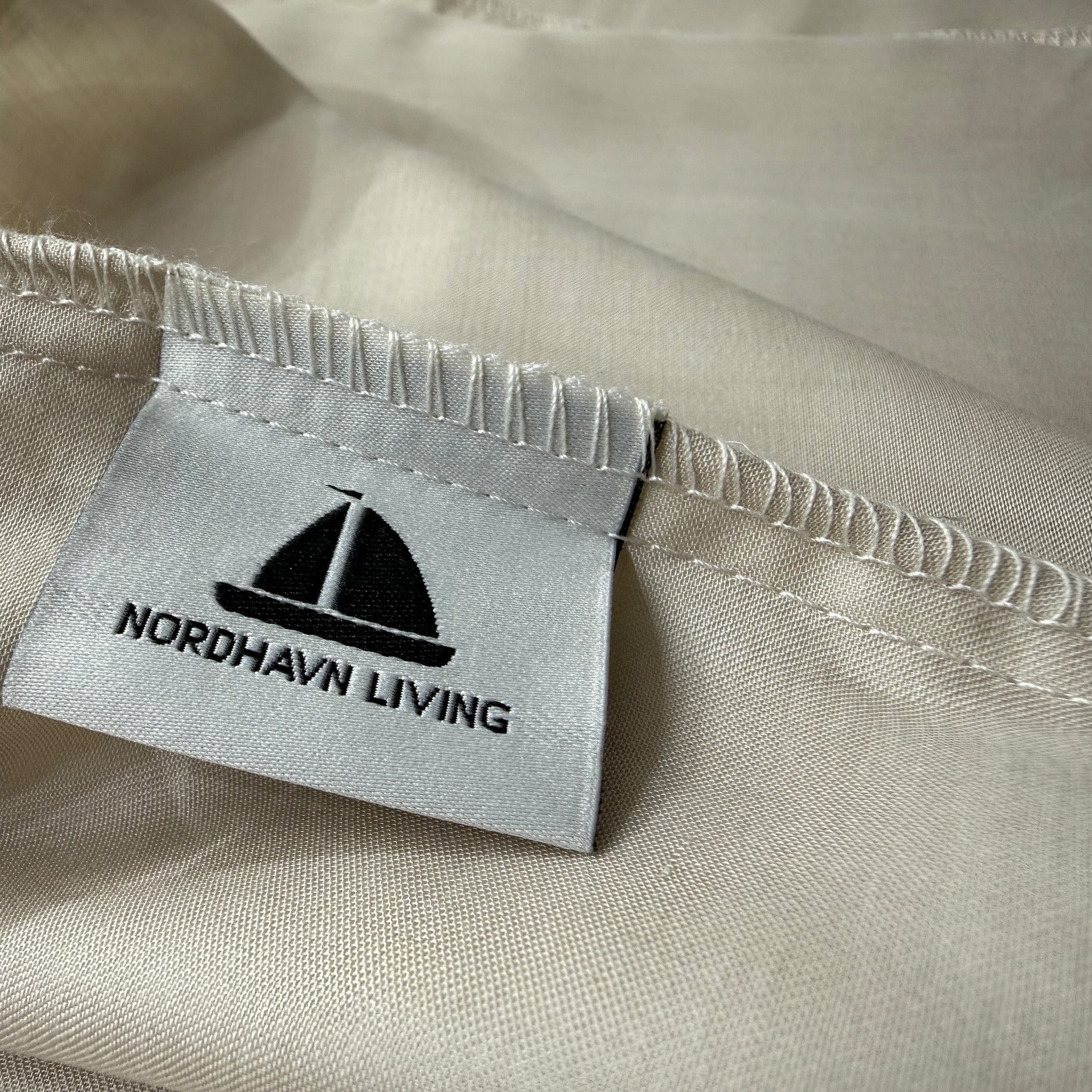 Nordhavn Living Aurora Satin Bettwäsche in Sandbeige (Drift Light): Detailaufnahme des eingenähten Marken-Labels mit Segelboot-Logo auf dem Tencel-Stoff.