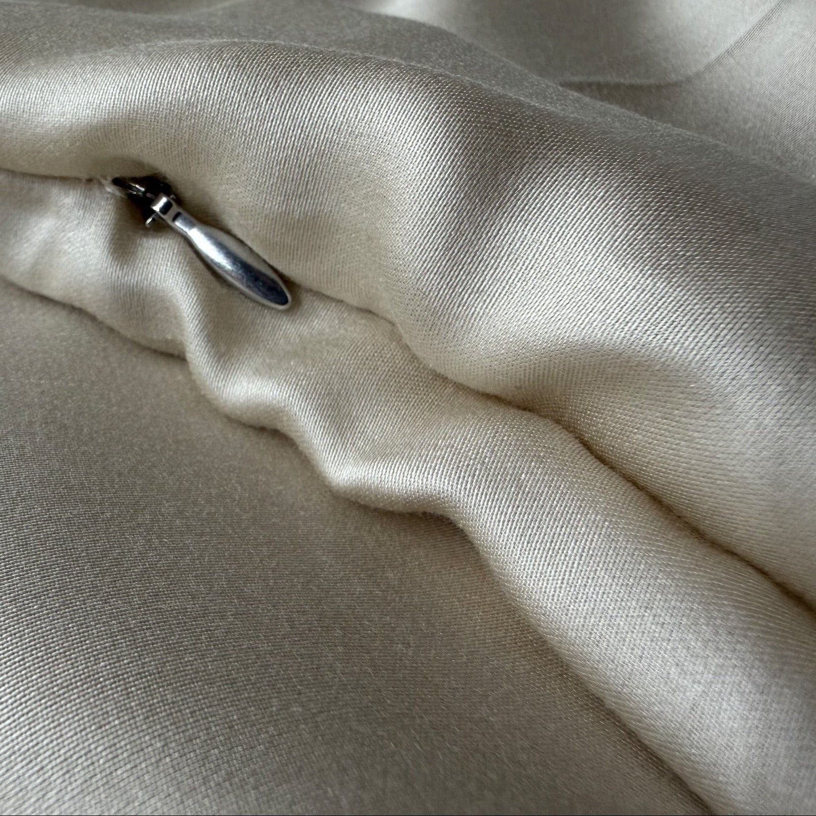 Nordhavn Living Aurora Satin Bettwäsche in Sandbeige (Drift Light): Detailansicht des robusten Metall-Schiebers, der für eine glatte Optik dezent unter einer Stofffalte verborgen liegt.