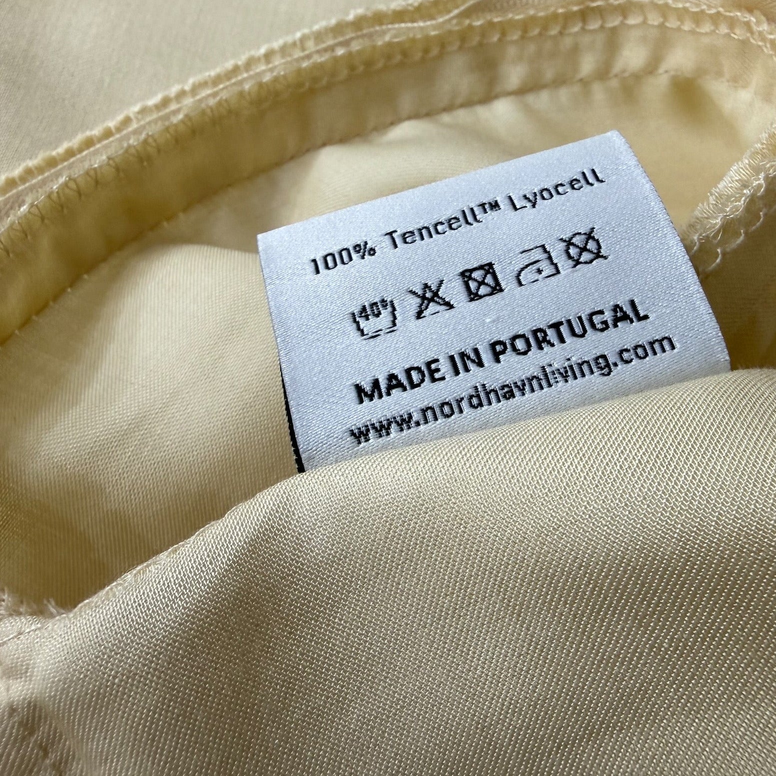 Nordhavn Living Aurora Satin Bettwäsche in Hellem Greige (Harvest Dust): Detailansicht des Einnähetiketts mit Pflegehinweisen, der Materialangabe 100% Tencel™ Lyocell und der Herkunft Made in Portugal.
