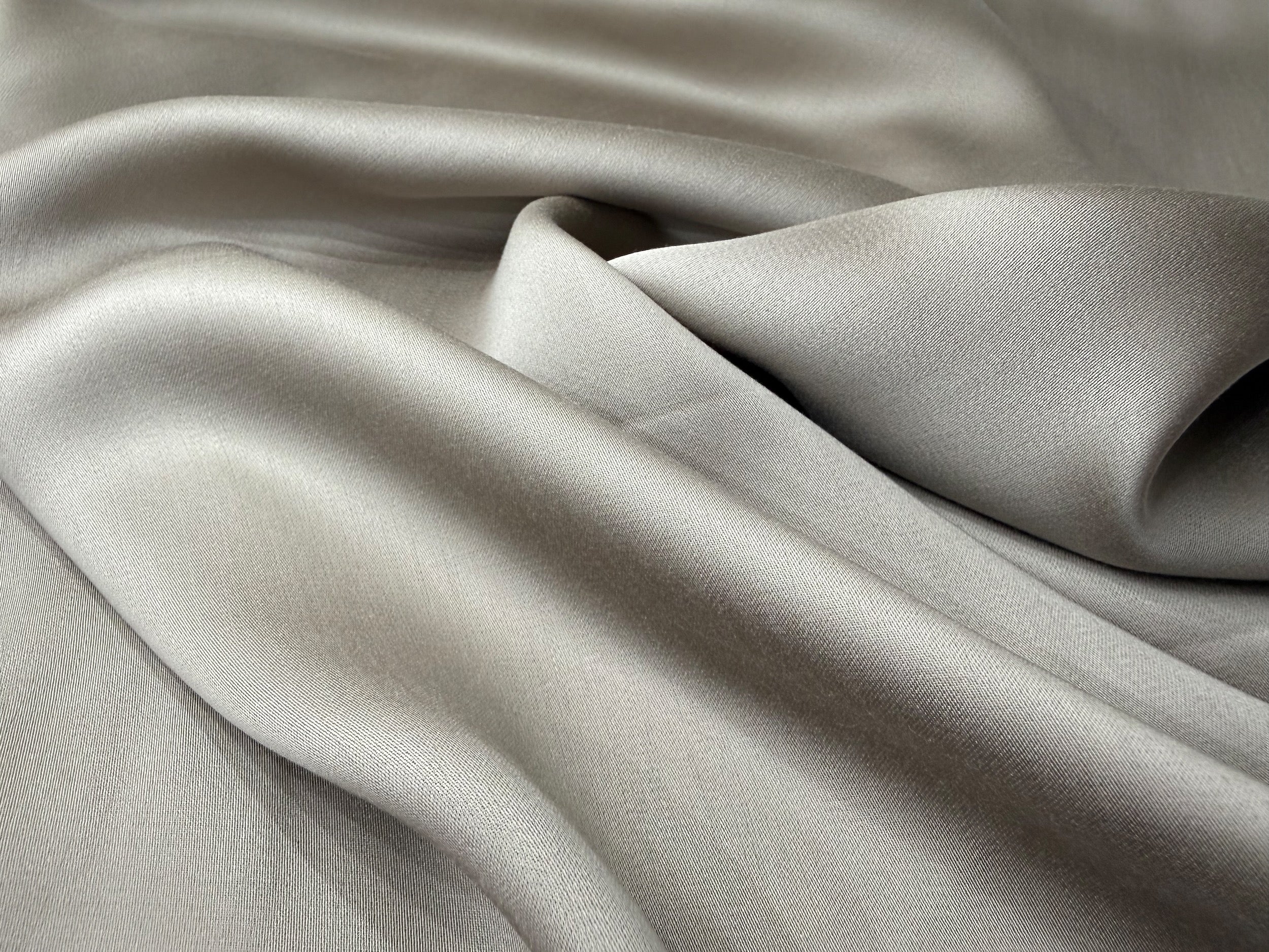 Nordhavn Living Aurora Satin Bettwäsche in Warmem Lehmgrau (Still Clay): Nahaufnahme der sanft fließenden Stoffwellen, die den eleganten Schimmer und die seidige Glätte des Tencel-Materials betonen.