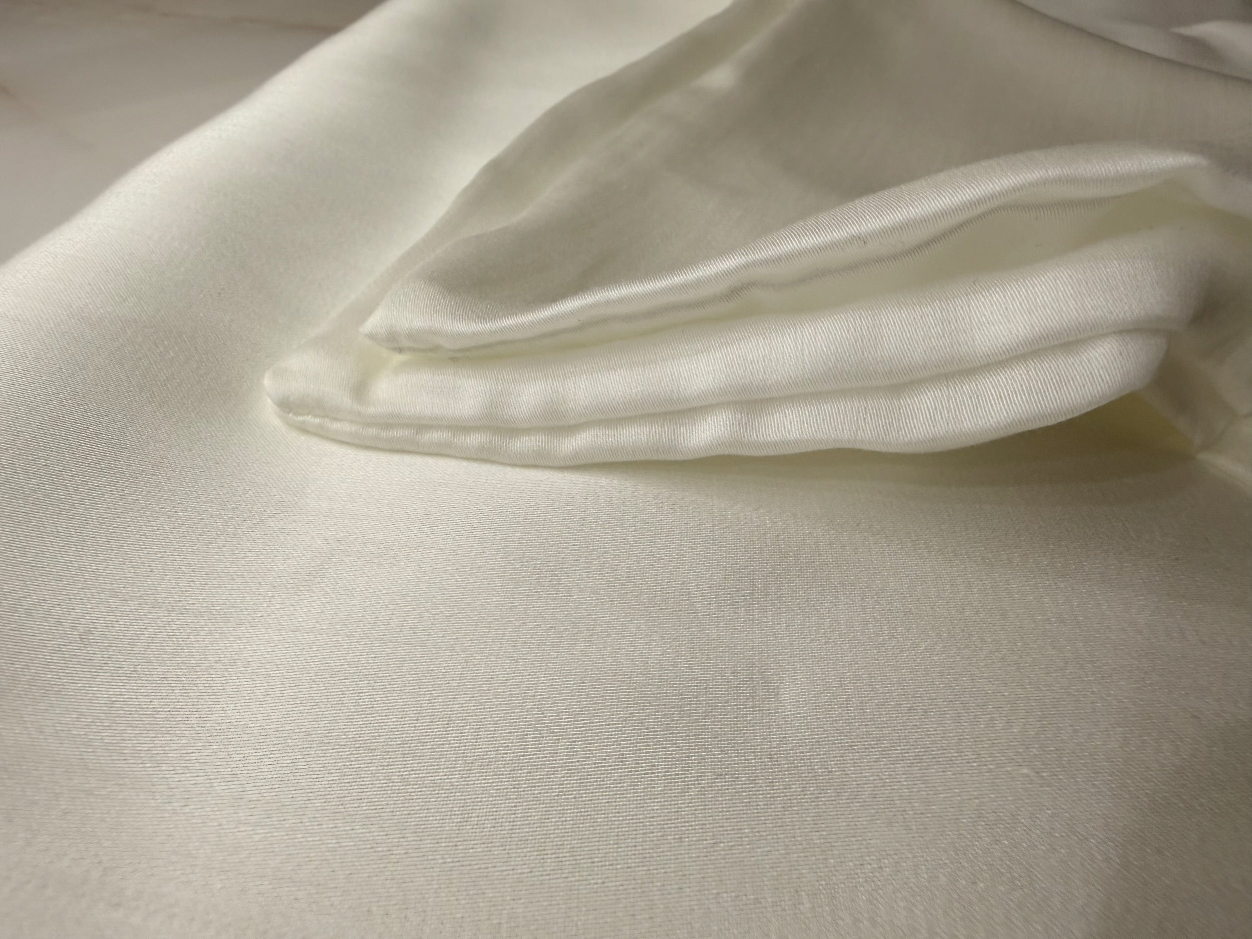 Nordhavn Living Aurora Satin Bettwäsche in Weiß (Quiet White): Detailansicht der feinen Nahtverarbeitung und der gefalteten Kante des Tencel-Stoffs.