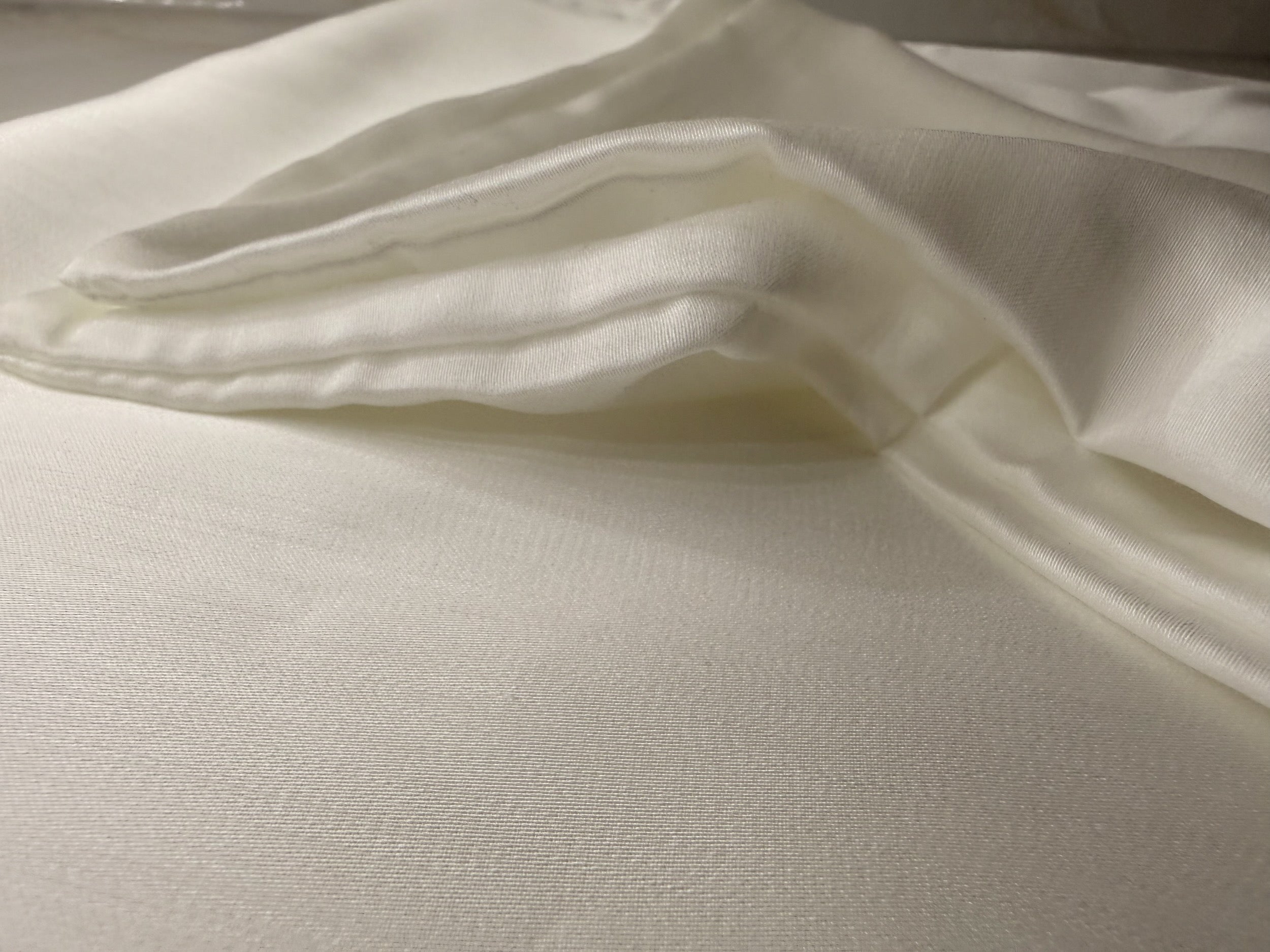 Nordhavn Living Aurora Satin Bettwäsche in Weiß (Quiet White): Nahaufnahme der weich gefalteten Stofflagen, die den edlen Schimmer und die Geschmeidigkeit des Tencel-Satins zeigen.