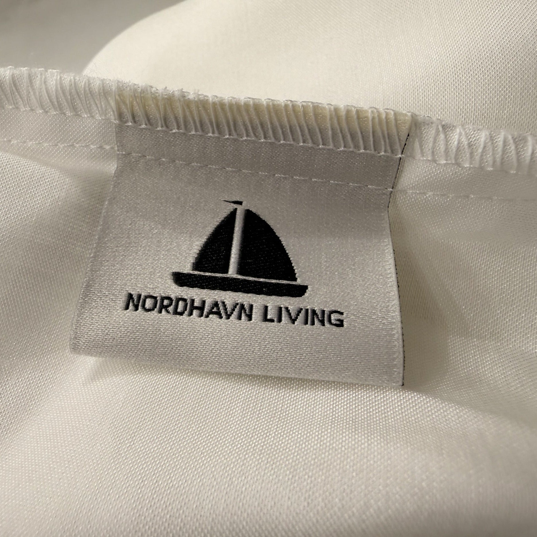 Nordhavn Living Aurora Satin Bettwäsche in Weiß (Quiet White): Detailaufnahme des eingenähten Marken-Labels mit Segelboot-Logo auf dem Tencel-Stoff.