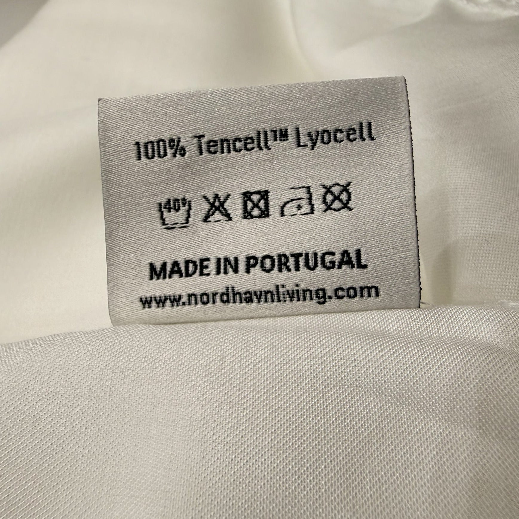 Pflegehinweis-Label an der weißen (Quiet White) Aurora Satin Bettwäsche: Bestätigung für 100% Tencel™ Lyocell und Made in Portugal Qualität.
